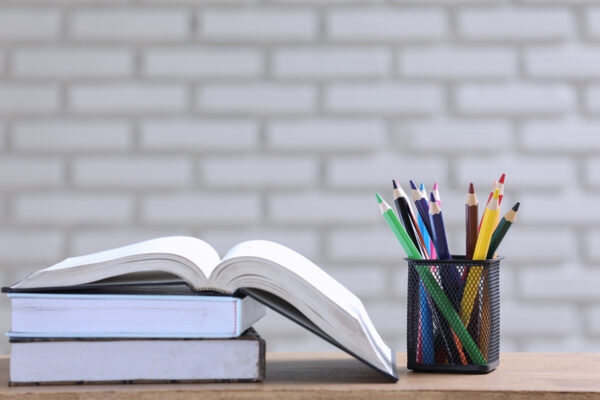 the pile of books, paper and pencil on the desk