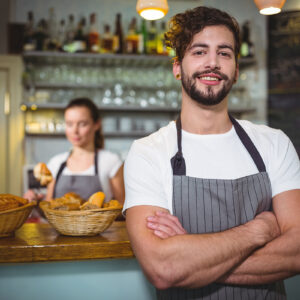 Smiling waiter standing with arms crossed in cafÃ©