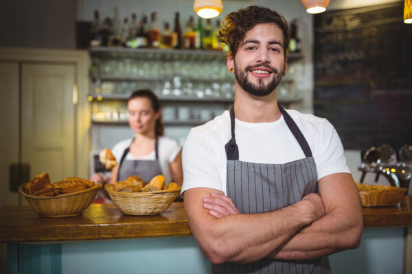 Smiling waiter standing with arms crossed in cafÃ©