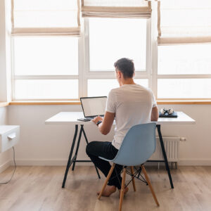 modern young handsome man in casual outfit sitting at table working on laptop, freelancer at home, view from back