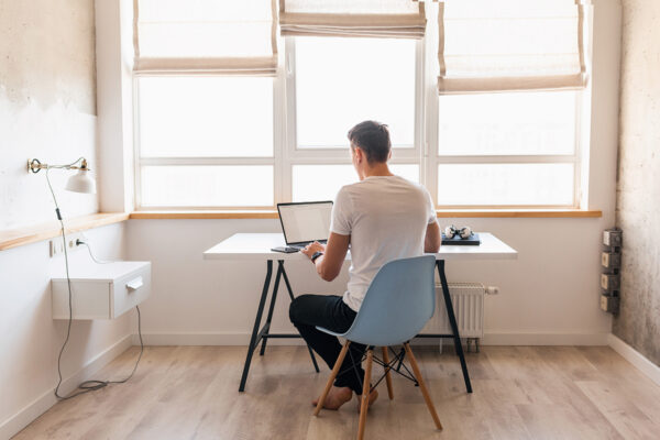 modern young handsome man in casual outfit sitting at table working on laptop, freelancer at home, view from back