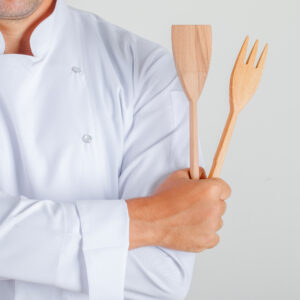Male chef holding kitchen utensils with crossed arms in uniform , front view.