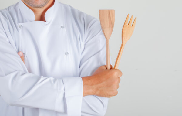 Male chef holding kitchen utensils with crossed arms in uniform , front view.