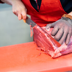 Woman cutting fresh meat in a butcher shop with metal safety mes