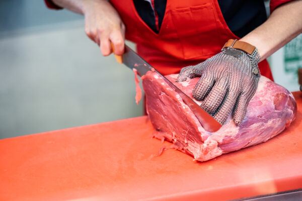 Woman cutting fresh meat in a butcher shop with metal safety mes